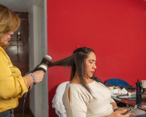 Hairdresser is styling a woman's hair in a beauty salon, using a blow dryer and round brush
